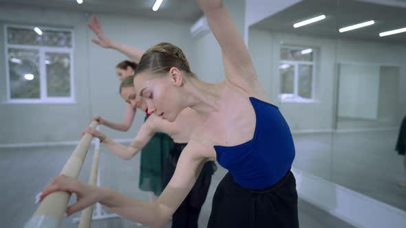 Slim Graceful Woman Moving in Fourth Ballet Position with Blurred Ballerinas Rehearsing