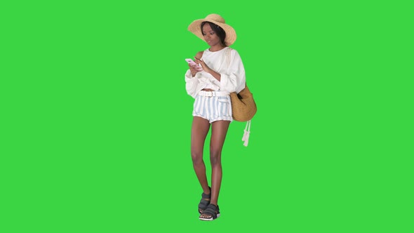 Smiling Young African American Woman in a Straw Hat Texting on Her Phone on a Green Screen, Chroma