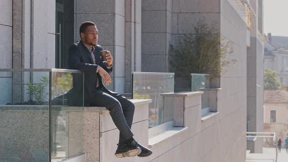 Carefree Smiling Young Mixed Race Man Wearing Suit Sitting Outdoors Near Office Enjoying Break