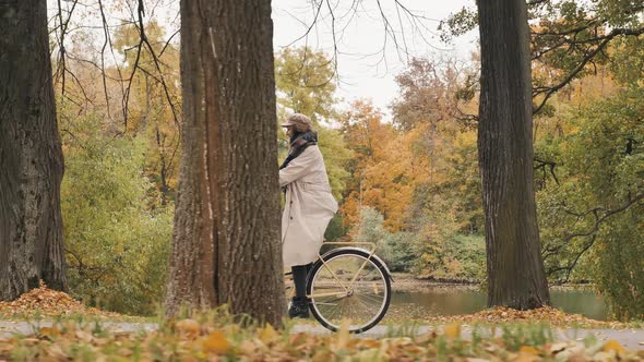 Young Woman Rides Bicycle Between Rows of Trees in Park