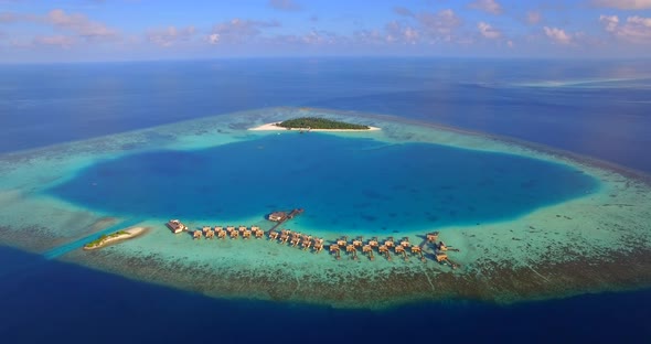 Aerial drone view of scenic tropical island and resort hotel with overwater bungalows in Maldives.
