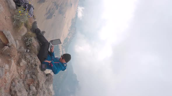 digital nomad, young latin man working on his laptop sitting on a rock in the mountain, backpacking,