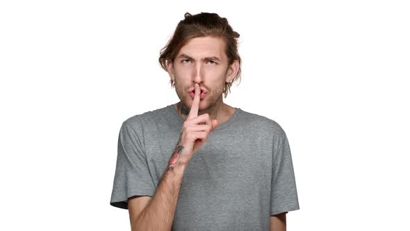 Portrait of Unshaved Guy Posing with Strict Gaze and Asking Keep Quiet Putting Index Finger on Lips