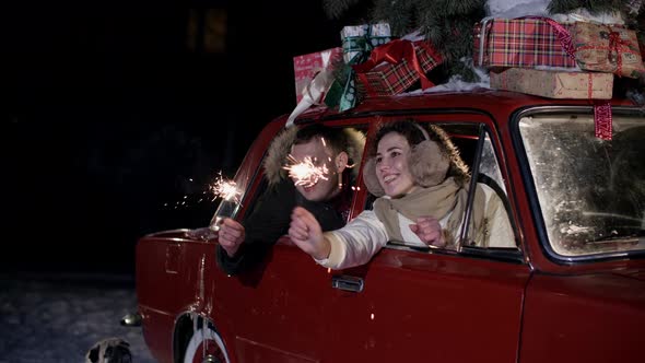 Happy Couple Sitting in Car and Holding Sparklers at Christmastime