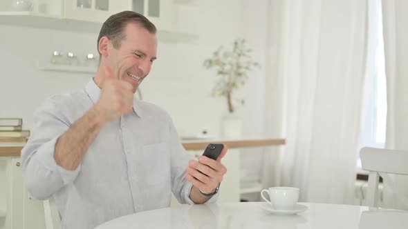 Middle Aged Man Celebrating Success on Smartphone at Home