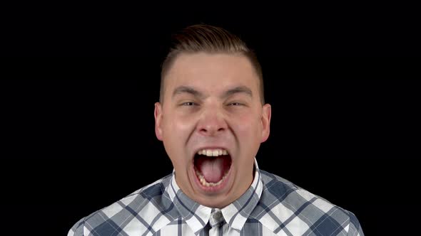 The Young Man Is Screaming. A Man Screams Strongly in a Shirt on a Black Background Closeup