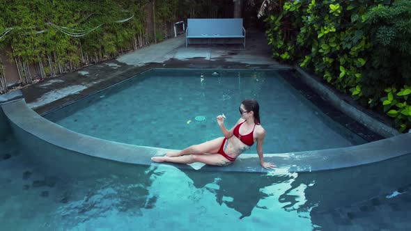 Young Woman in Red Bikini Lays on Blue Water Pool