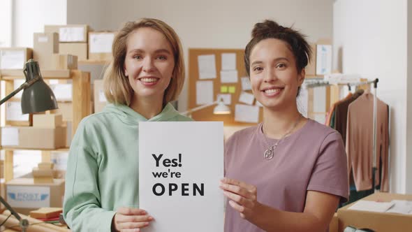 Two Happy Female Coworkers Posing with We Are Open Poster