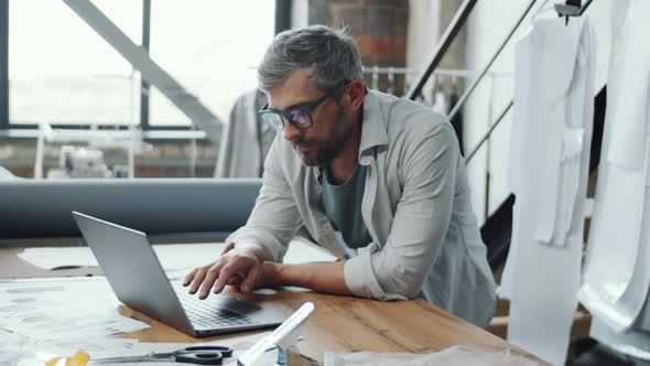 Portrait of Handsome Tailor Using Laptop and Posing for Camera at Work