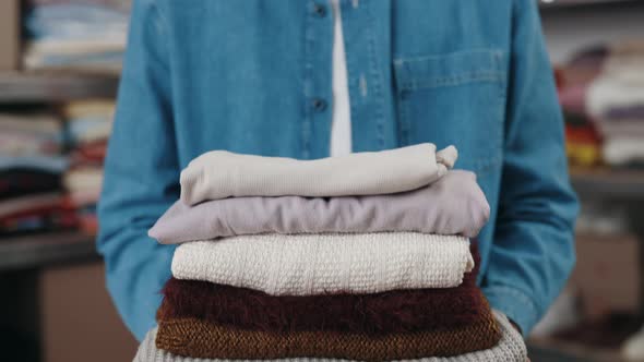 Multiracial Male Worker Stretching to the Camera Stack of Clothes While Working at the Donating