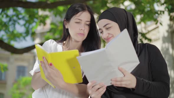 Portrait of Absorbed Happy Women Discussing Homework at University Yard. Young Beautiful Caucasian