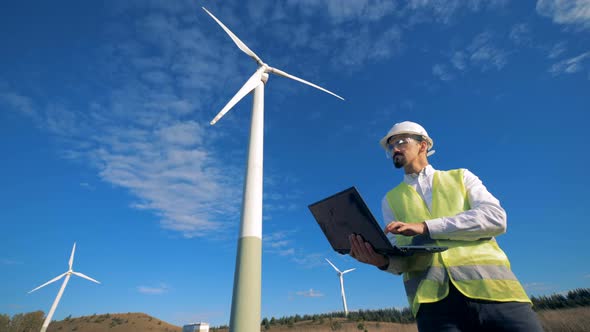 Functioning Wind Turbine Towers and an Energetics Worker Standing Beside Them with a Laptop