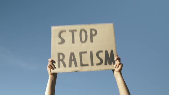 Poster STOP RACISM against blue sky. Hands against blue sky holding sign "Stop Racism". 