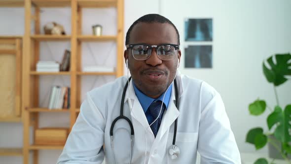 Front View of Young Male Doctor Talking with Smile While Sitting at Table in Modern Clinic Spbas