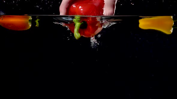 Hand pulling a bell pepper out of water in slow motion.