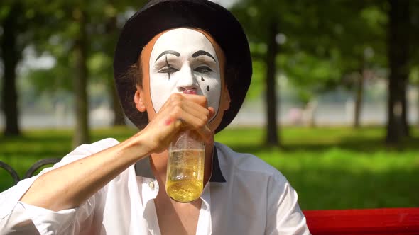 Mime in a Black Hat Drinks Alcohol Outdoors. Bad Habits