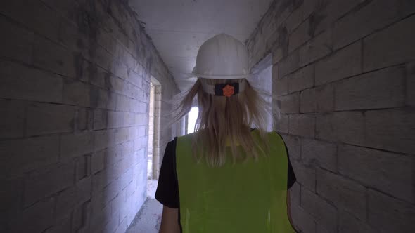 a woman in white helmet walks along corridor of construction site, building.