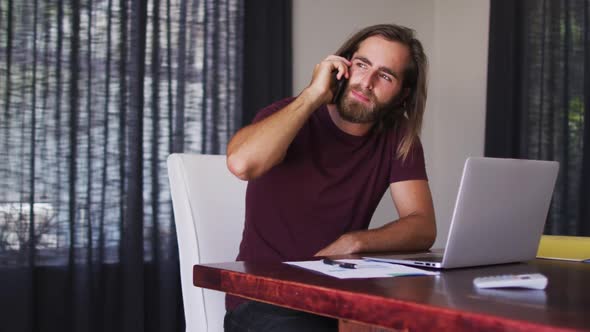 Caucasian man talking on smartphone while using laptop at home