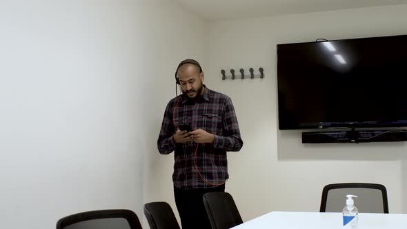 An Indian man pacing up and down a boardroom talking to a colleague on his mobile phone, the man foc