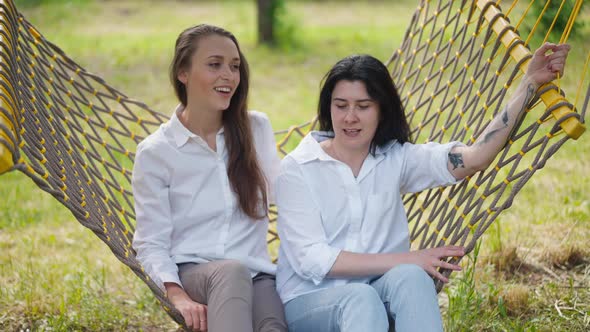 Two Young Caucasian Women Swinging Sitting in Hammock Talking in Slow Motion