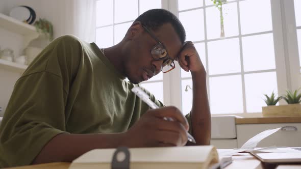 AfricanAmerican Man Works at Home at a Desk or a Student Takes Notes on a Lecture Makes Notes in a