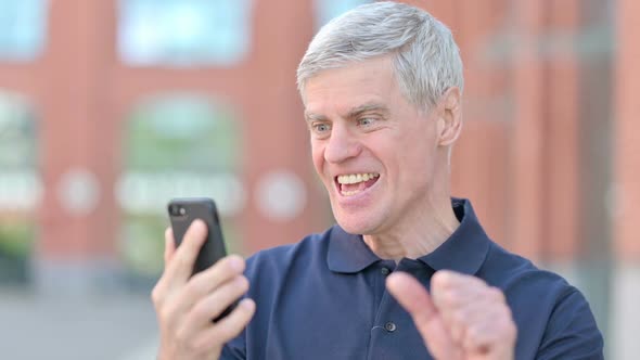 Outdoor Portrait of Middle Aged Man Celebrating Success on Smartphone