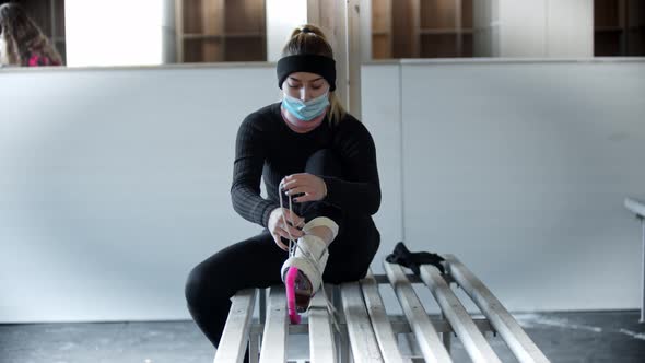 Ice Skating  Young Woman in Medicine Mask Ties Shoelaces on White Skates