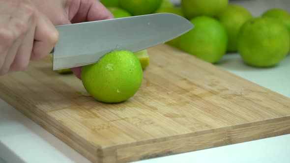 Hand Slicing fresh Lime With Knife On Wooden Board In Kitchen