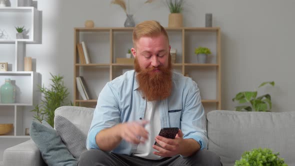 Young Handsome Redhead Man Sit on Sofa with Smartphone Write Message Use Messenger Edate Services