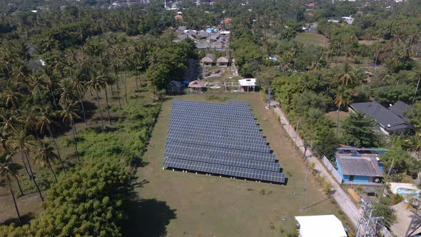 Aerial flyover solar panels area surrounded by tropical palm trees during sunlight on Gili Air Islan