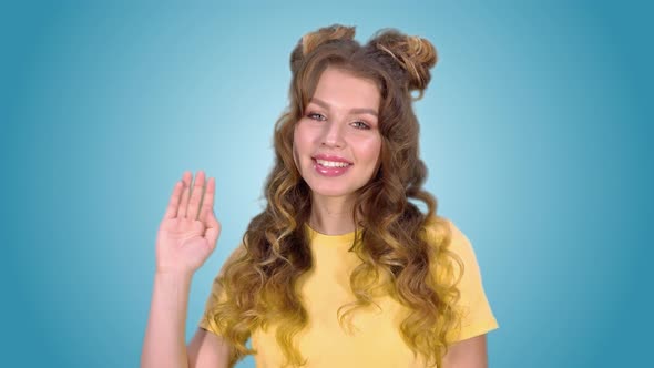 Beautiful Young Girl in a Yellow Shirt Waving Her Hand and Smiling While Looking Into the Camera