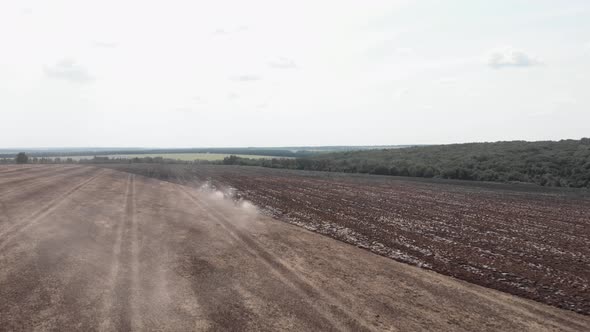 Moving tractor with plow raising dust on field. Farmer plowing farm field.