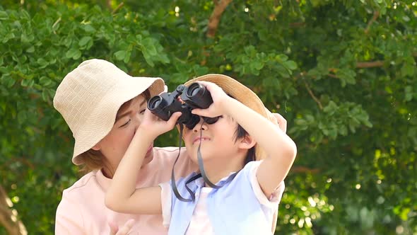 Asian Mother And Her Son Using Binocular And Pointing On Summer Day