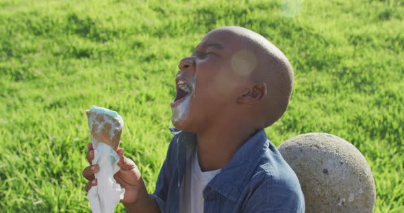 Video of happy african american boy eating ice creams and laughing on sunny day