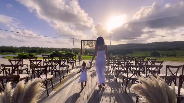 A Little Girl in a White Dress Holds the Hand of a Bride in a Wedding Dress and Walks to the Wedding