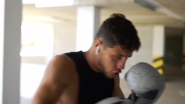 The Man Executes Strong Blows in the Boxing Bag at the Parking Zone Gym Closeup