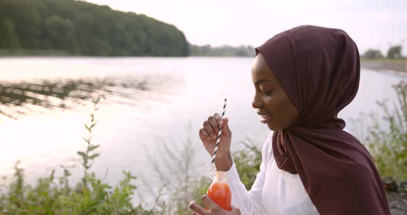 Muslim Black Woman Drinking Coktail at River Bank