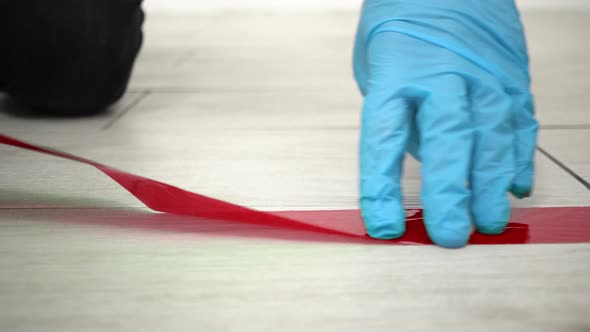 Man in medical gloves putting red tape floor markings for social distance indoors