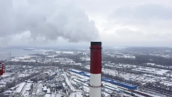 Smoking Factory Chimney Against the Background of Big Industrial City Covered with Snow