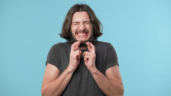 Portrait of Joyful Young Man 20s Squinting Eyes with Keeping Fingers Crossed and Begging God Please