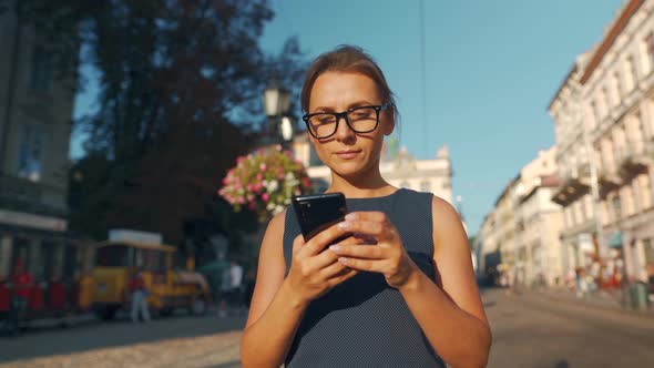 Woman Walking Down an Old Street and Using Smartphone at Sunset