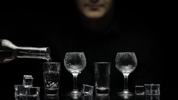 Barman Pour Frozen Vodka From Bottle Into Glasses with Ice. Black Background