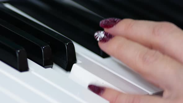 Close-up of a woman's hand with a manicure plays the piano keys.