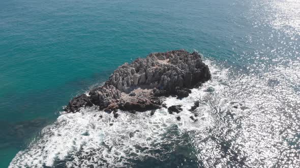 Lonely stone cliff with waves break on rock and create white foam