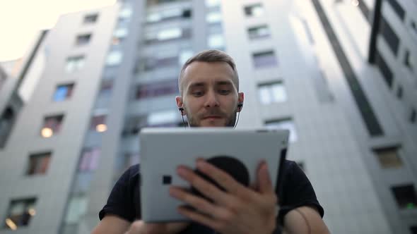 A man, using a tablet in front of high building