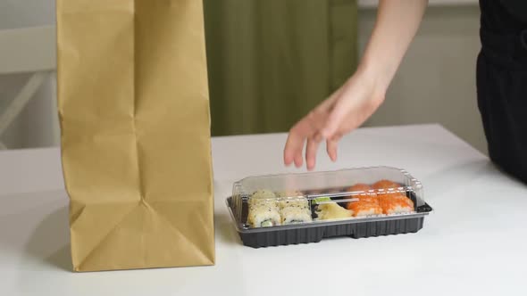 Food delivery concept: woman takes out delivered sushi boxes with japanese food. Take away food.