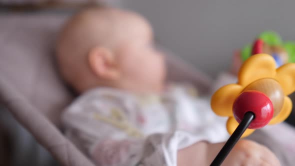 Baby Girl Sitting In Bouncer And Playing With Colorful Toys.