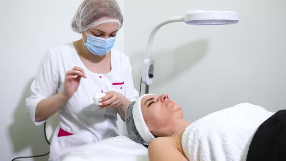 Beautician Applying Cream on Face of Female Customer in Wellness Salon