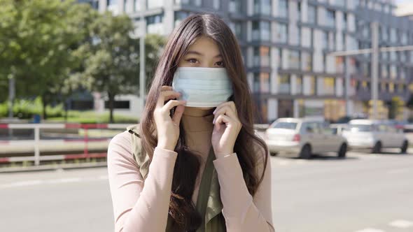 Young Asian Woman Puts Face Mask Looks Camera Street Urban Area