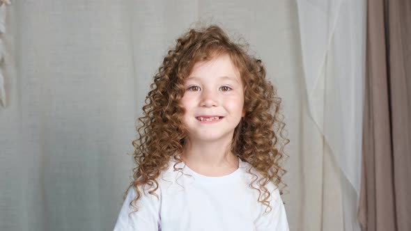 Curly Reddishbrown Haired Preschooler Girl in Shirt Smiles